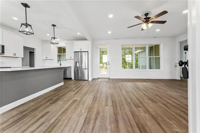 a view of an empty room and kitchen with wooden floor and a ceiling fan