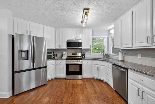 a kitchen with granite countertop a refrigerator stove a sink and dishwasher with wooden floor