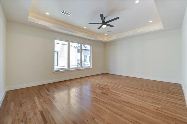 an empty room with wooden floor ceiling fan and windows