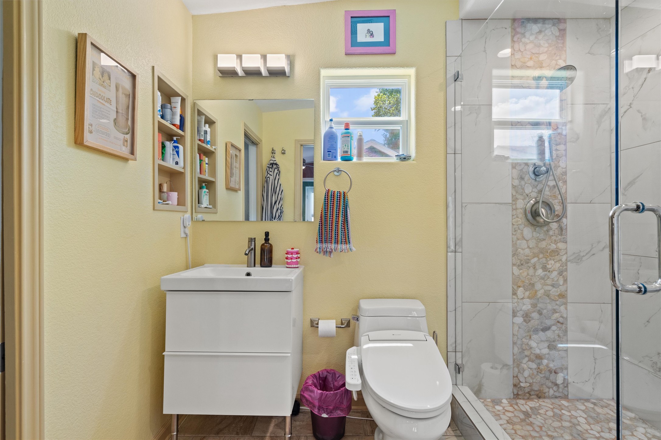 1147 Webberville Road Austin, TX 78721 - Photo 23 of 37 A streamlined vanity and modern commode complement a glass-enclosed shower with a river rock tile accent strip.