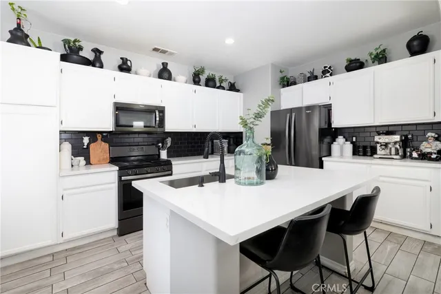 a kitchen with stainless steel appliances a stove a sink a refrigerator and white cabinets with wooden floor