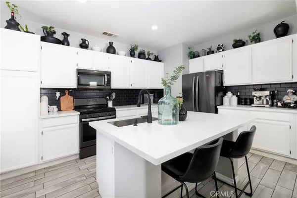 a kitchen with stainless steel appliances a stove a sink a refrigerator and white cabinets with wooden floor