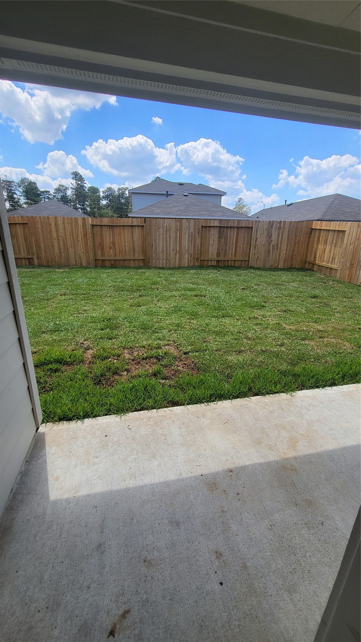 23835 Sunland Park Spring, TX 77373 - Photo 14 of 14 This is a view from a back patio showing a flat, grassy backyard enclosed by a tall wooden privacy fence. The sky is clear with a few clouds, suggesting a pleasant, sunny environment.