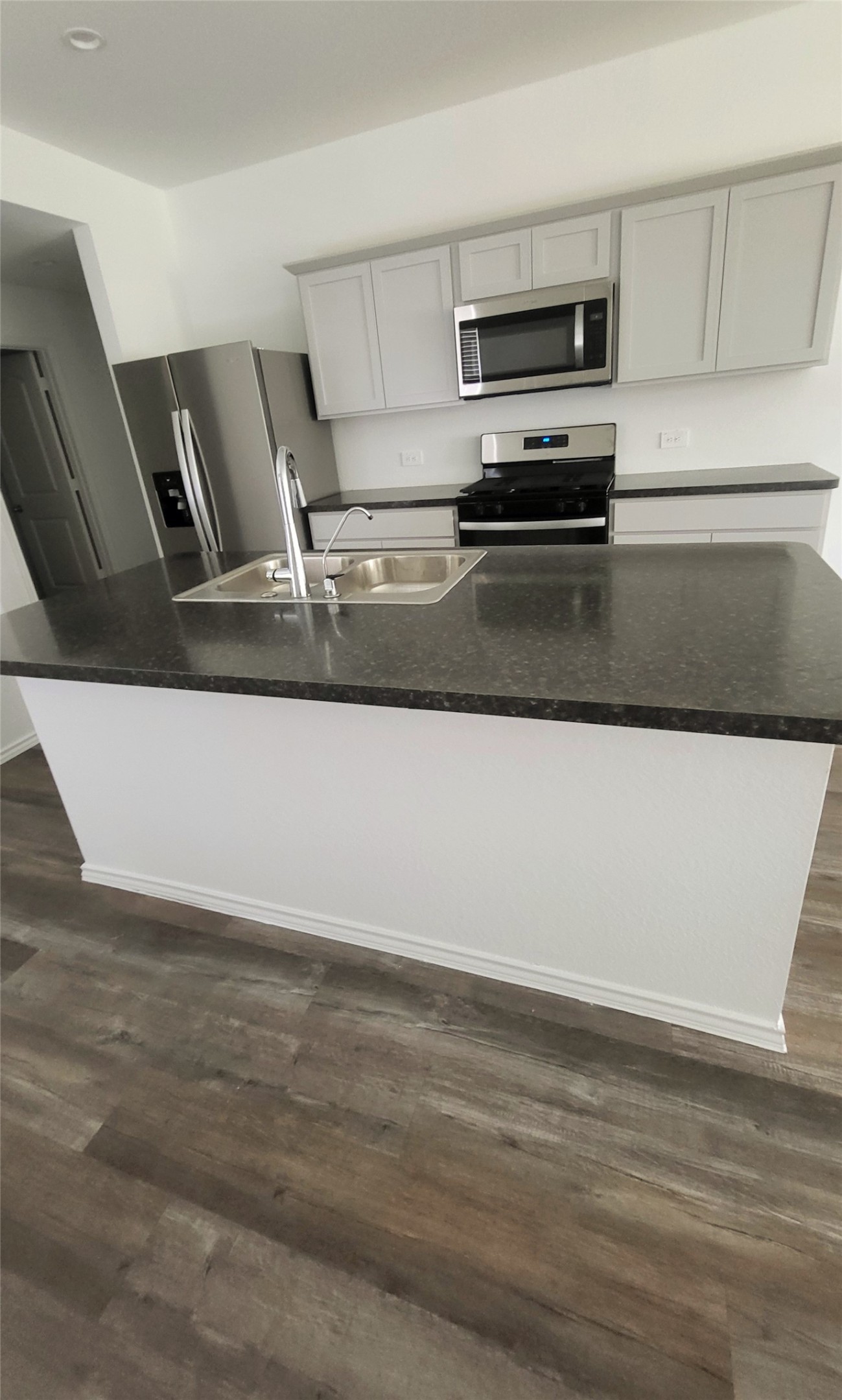 23835 Sunland Park Spring, TX 77373 - Photo 3 of 14 Modern kitchen featuring stainless steel appliances, white cabinetry, a large island with a sink, and wood-look flooring.