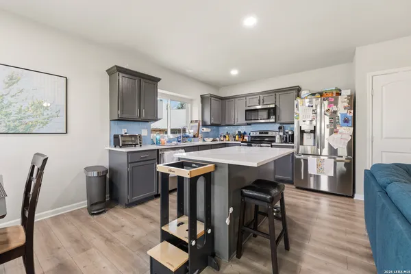a kitchen with stainless steel appliances granite countertop a refrigerator a sink dishwasher a stove a dining table and chairs with wooden floor