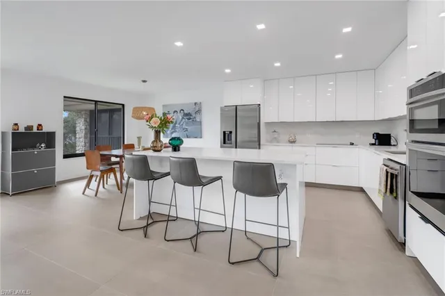 a kitchen with stainless steel appliances kitchen island granite countertop a sink a stove a refrigerator and chairs