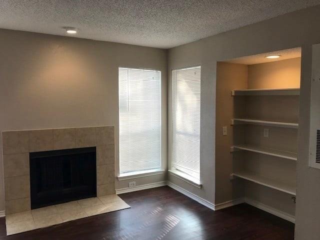 Unfurnished living room featuring a tiled fireplace, dark wood-style flooring, and a textured ceiling