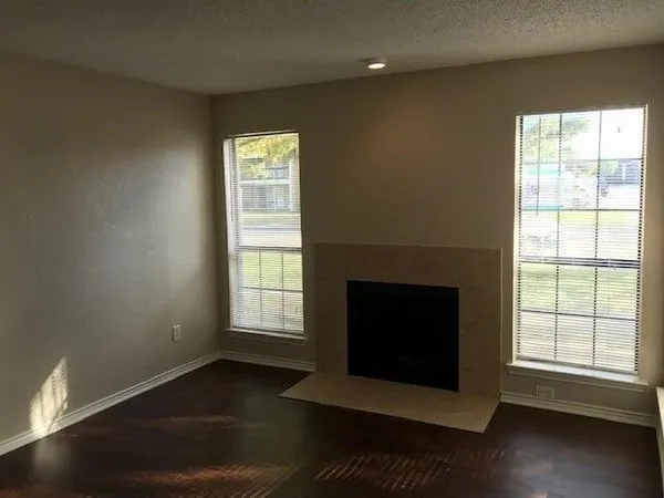 an empty room with wooden floor fireplace and windows