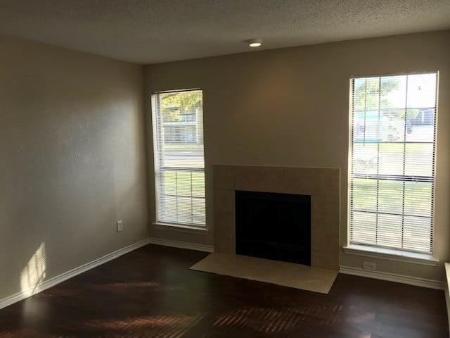 8005 Rothington Road, Unit 53 Dallas, TX 75227 - Photo 2 of 11 Unfurnished living room featuring a tiled fireplace, a textured ceiling, and dark wood-style flooring