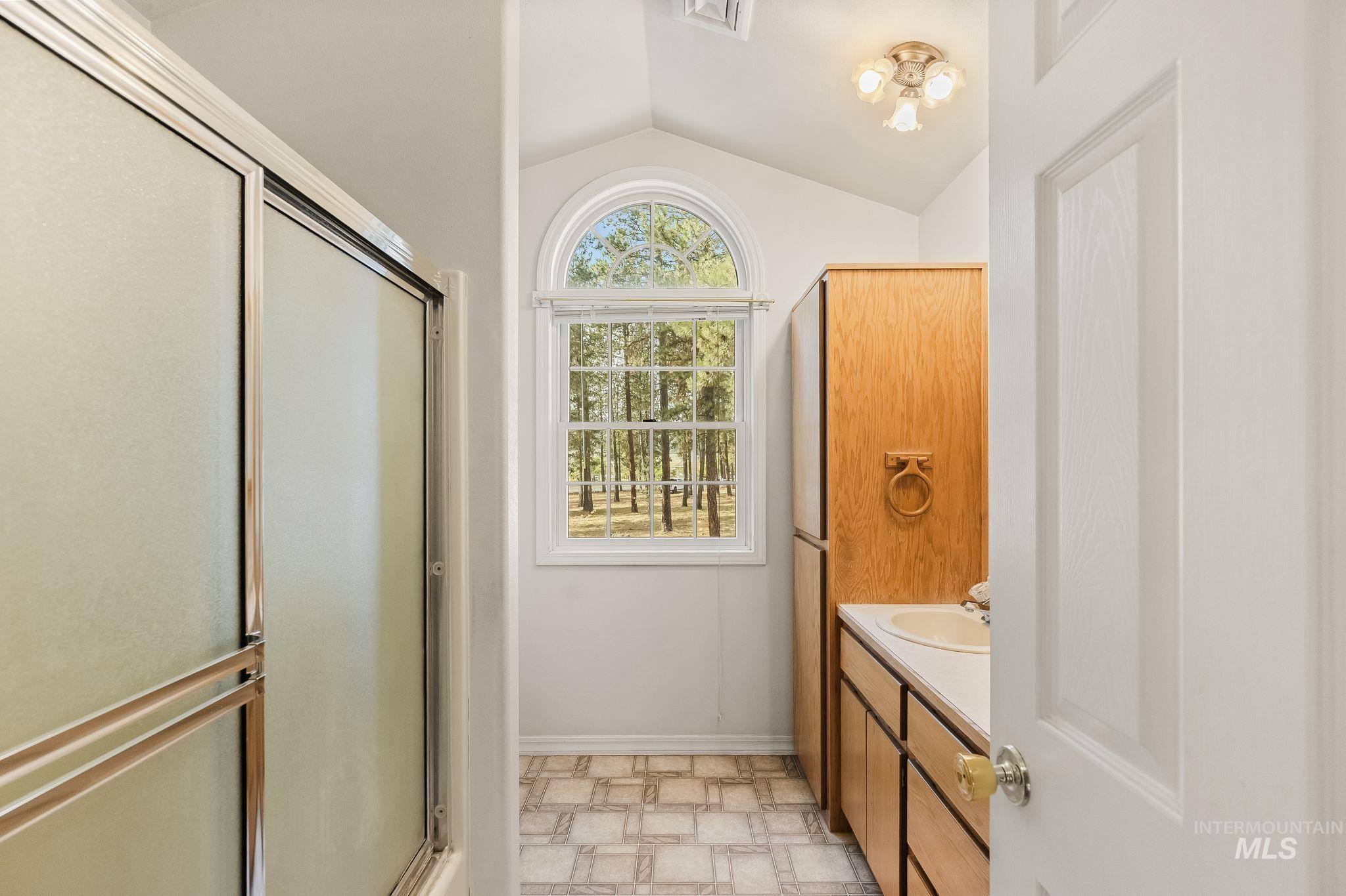 1820 Winchester Road Winchester, ID 83555 - Photo 23 of 50 Shower enclosure with frosted glass, arched window, wood-finish cabinetry, and vanity with integrated sink