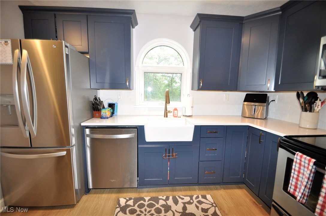 467 Cahoon Road Bay Village, OH 44140 - Photo 15 of 41 Kitchen featuring stainless steel appliances, light wood-style flooring, blue cabinetry, and backsplash