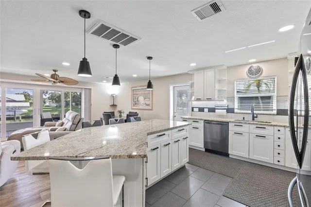 a large kitchen with granite countertop lots of white cabinets a sink dishwasher and a stove with wooden floor