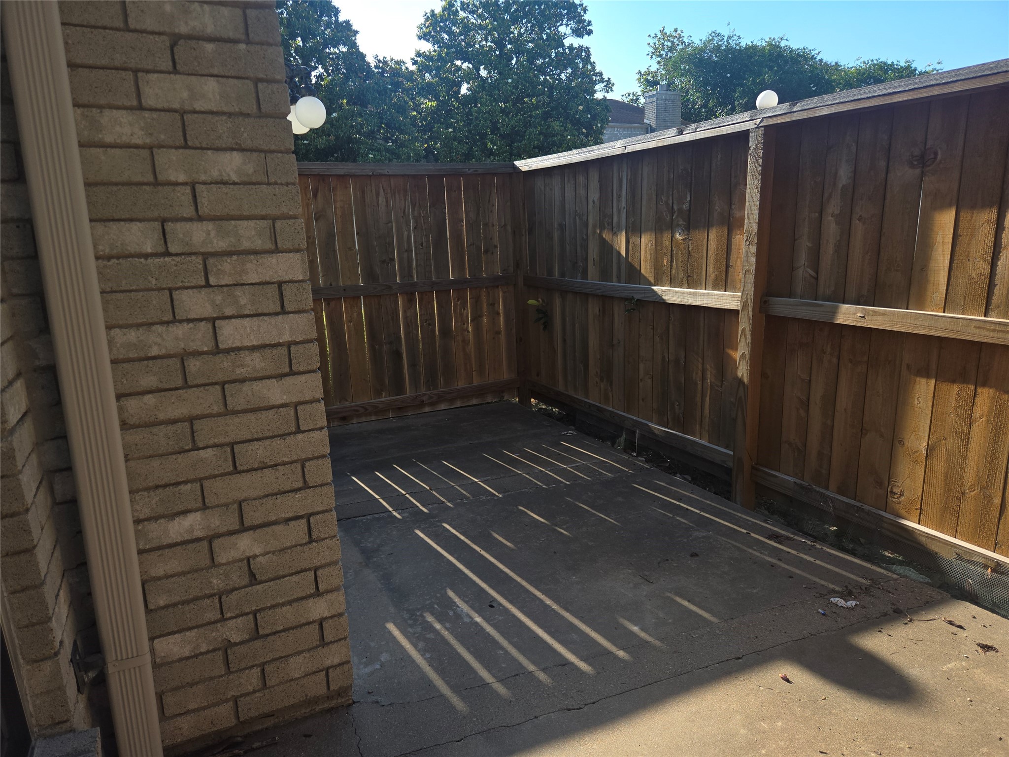 3780 Tanglewilde Street, Unit 501 Houston, TX 77063 - Photo 21 of 26 This photo shows a small outdoor patio area with a concrete floor, surrounded by a wooden privacy fence and partially shaded by nearby trees. Ideal for a cozy seating area or small garden space.