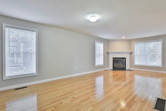 an empty room with wooden floor fireplace and windows