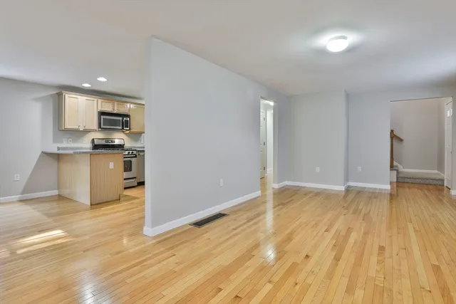 a view of empty room with wooden floor and kitchen