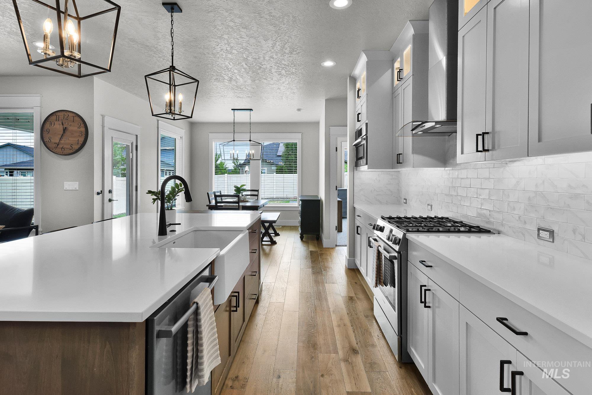 5676 East Zaffre Ridge Street Boise, ID 83716 - Photo 14 of 50 Expansive kitchen featuring a large island with a farmhouse sink, light wood-finish flooring, white cabinetry with black hardware, white countertops, and a subway tile backsplash