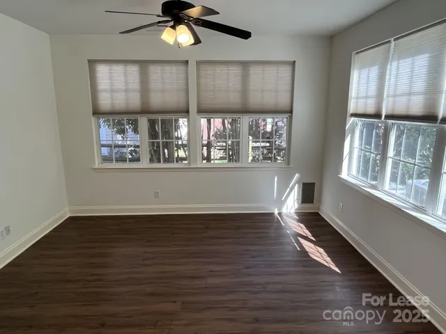an empty room with wooden floor fan and windows