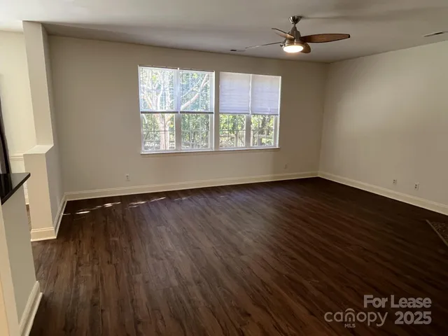 an empty room with wooden floor chandelier fan and windows