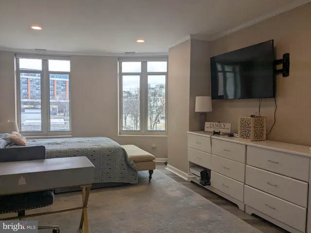 a bedroom with a bed a table and three windows