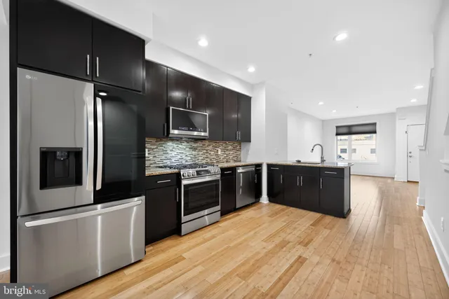 a large kitchen with stainless steel appliances kitchen island granite countertop a refrigerator a sink dishwasher and a stove with wooden floors