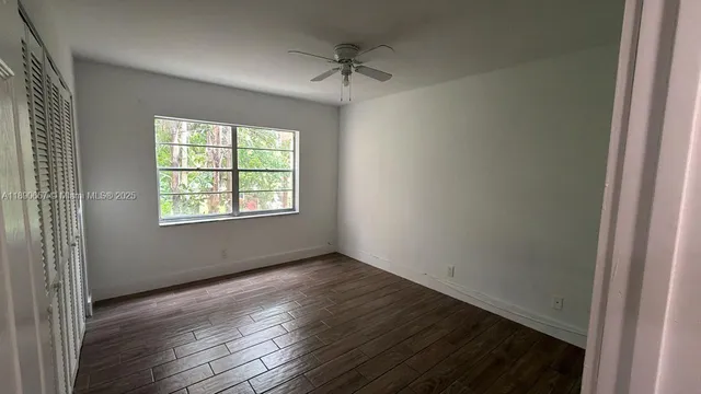 an empty room with wooden floor fan and windows