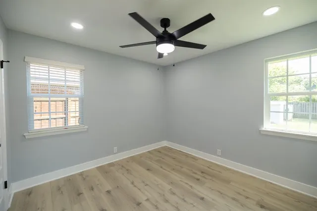 an empty room with wooden floor fan and windows