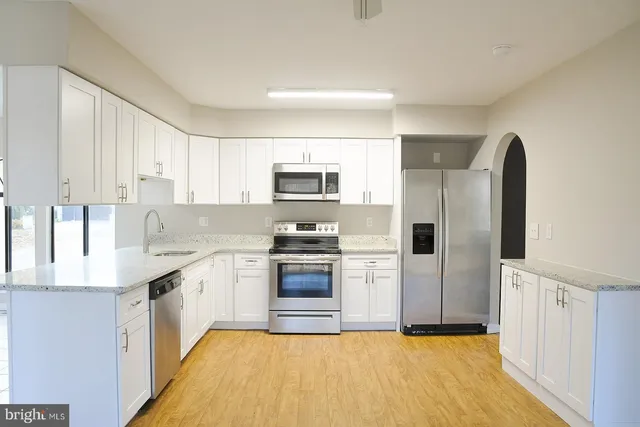 a kitchen with stainless steel appliances granite countertop a stove top oven a sink dishwasher a refrigerator and a dining table with wooden floor