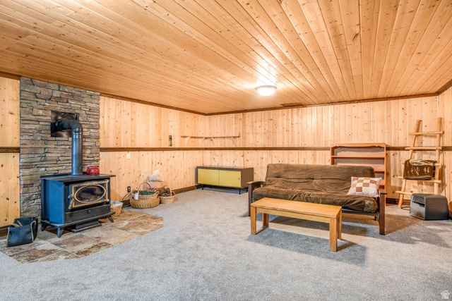 48 South Sage Road Pine Valley, UT 84781 - Photo 43 of 61 Spacious room featuring wood paneling on walls and ceiling, a stone-clad accent wall with a freestanding stove, light gray carpet flooring, and a flush-mount ceiling light fixture