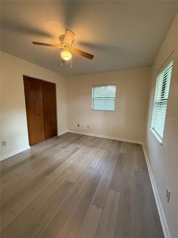 an empty room with wooden floor chandelier fan and windows