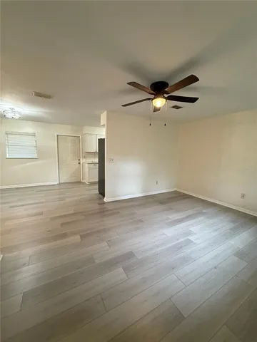an empty room with wooden floor fan and windows