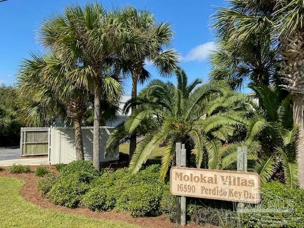a sign that is sitting in front of a house with a tree
