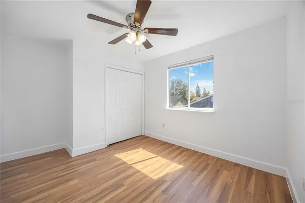 an empty room with wooden floor chandelier fan and windows