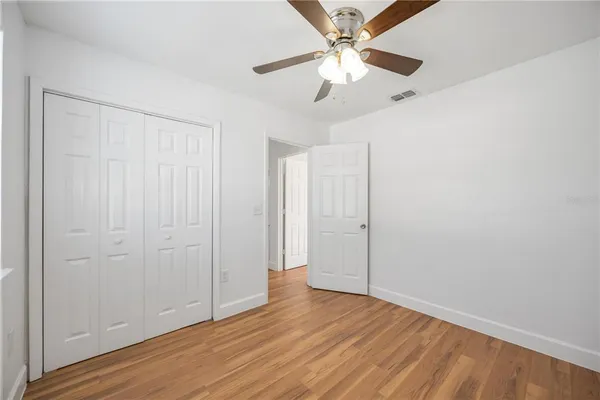 an empty room with wooden floor fan and windows