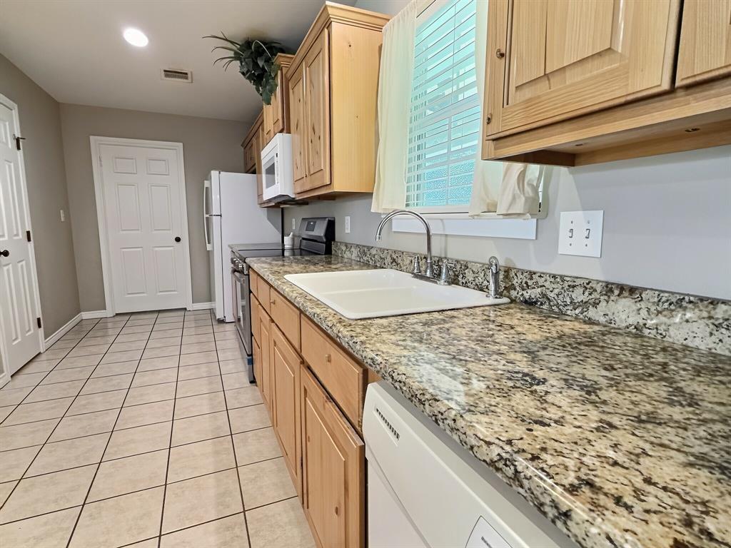 313 East River Oaks Road Early, TX 76802 - Photo 8 of 34 Kitchen featuring light wood cabinetry, stone countertops, a stainless steel faucet, and tile flooring