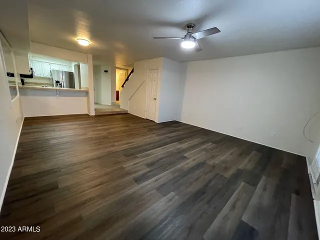 an empty room with wooden floor kitchen view and a ceiling fan