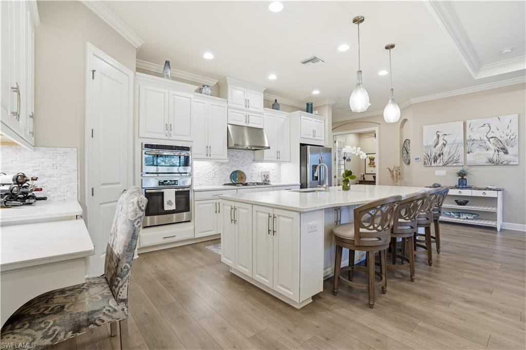 8665 Dilillo Court Naples, FL 34119 - Photo 6 of 42 a kitchen with stainless steel appliances kitchen island granite countertop a table chairs sink and cabinets