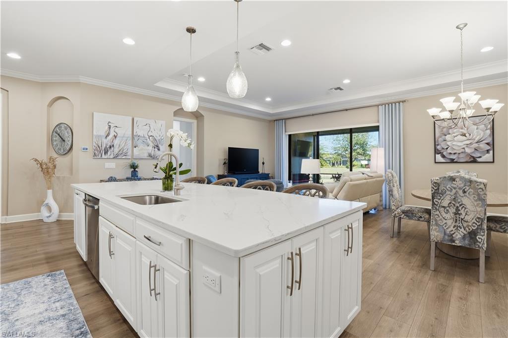 8665 Dilillo Court Naples, FL 34119 - Photo 9 of 42 a large white kitchen with a large island oven a sink dishwasher a dining table and chairs with wooden floor
