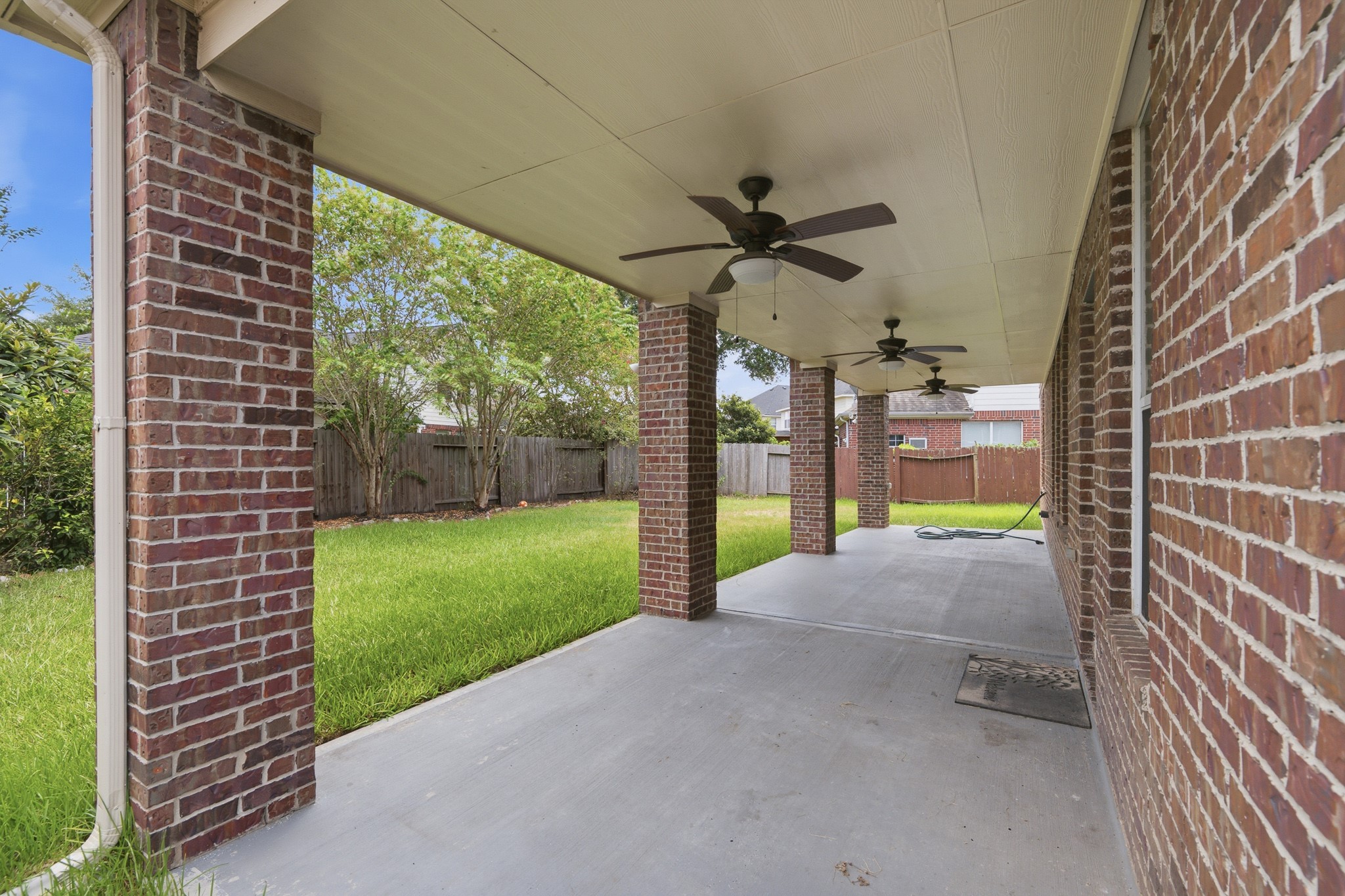 2117 Rushing Spring Drive Pearland, TX 77584 - Photo 40 of 42 Spacious covered patio with elegant brick columns and ceiling fans, overlooking a lush, fenced backyard perfect for outdoor relaxation.
