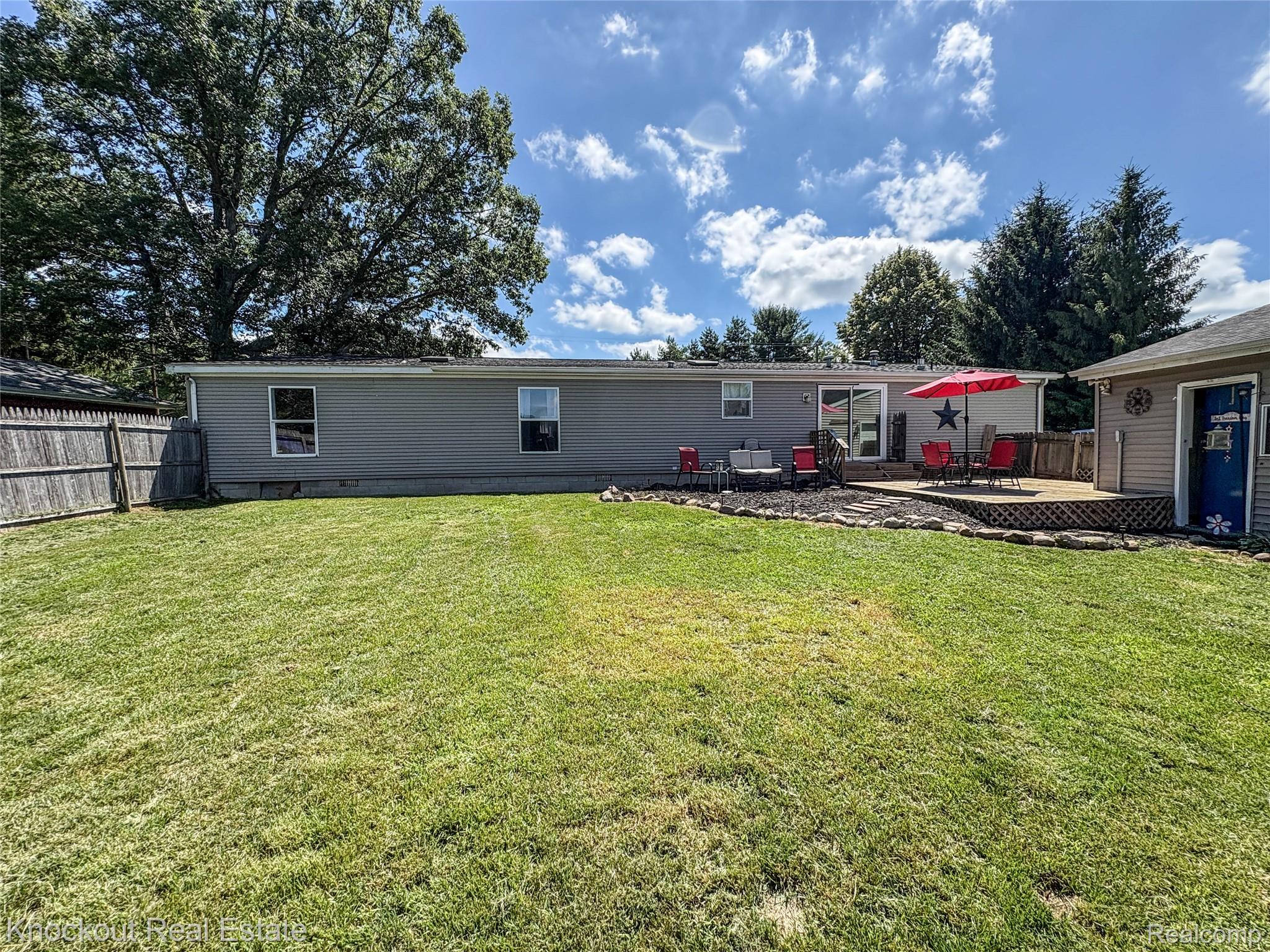 7760 Bell Road Birch Run, MI 48415 - Photo 57 of 68 Expansive backyard featuring a large wooden deck, sliding glass door access to the interior, and a detached outbuilding with a distinct blue door