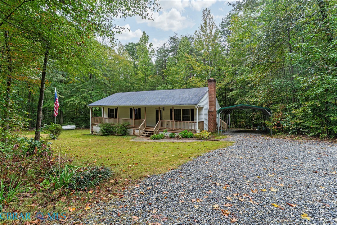 View of front facade featuring covered porch, a front yard, driveway, a chimney, and a carport