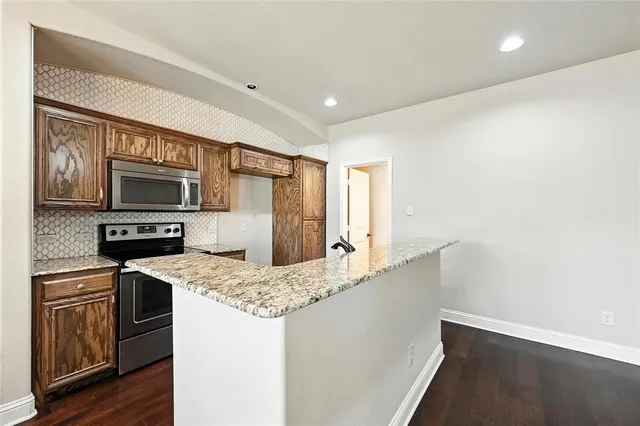 a kitchen with stainless steel appliances granite countertop a refrigerator a stove and a sink with wooden floor