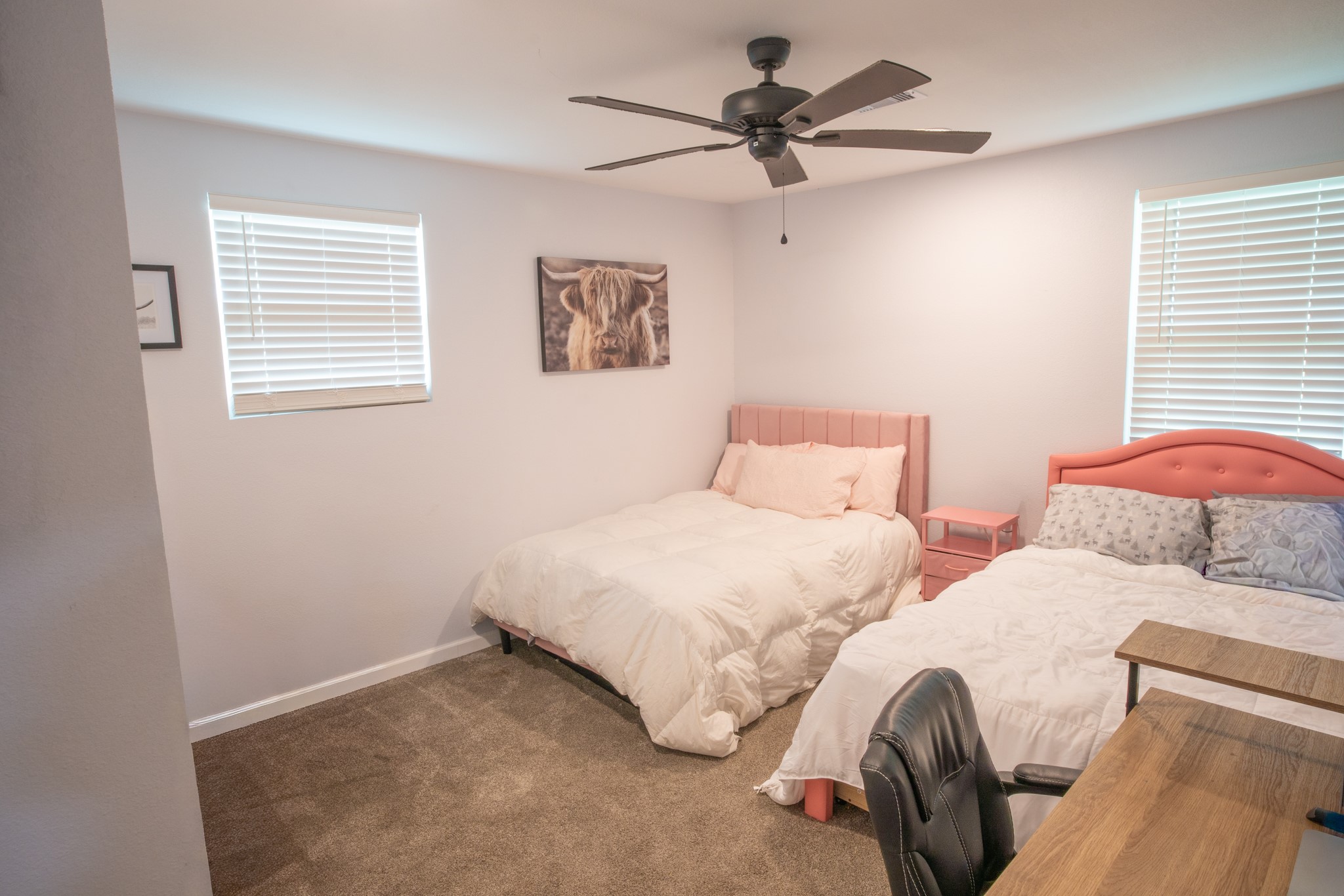 846 South Anderson Street Angleton, TX 77515 - Photo 19 of 30 This cozy bedroom features room for two beds, a ceiling fan, and natural light from two windows. There is room for a small bedside table and a desk with a chair, creating a functional and inviting space.