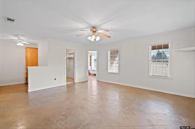 an empty room with chandelier fan and windows
