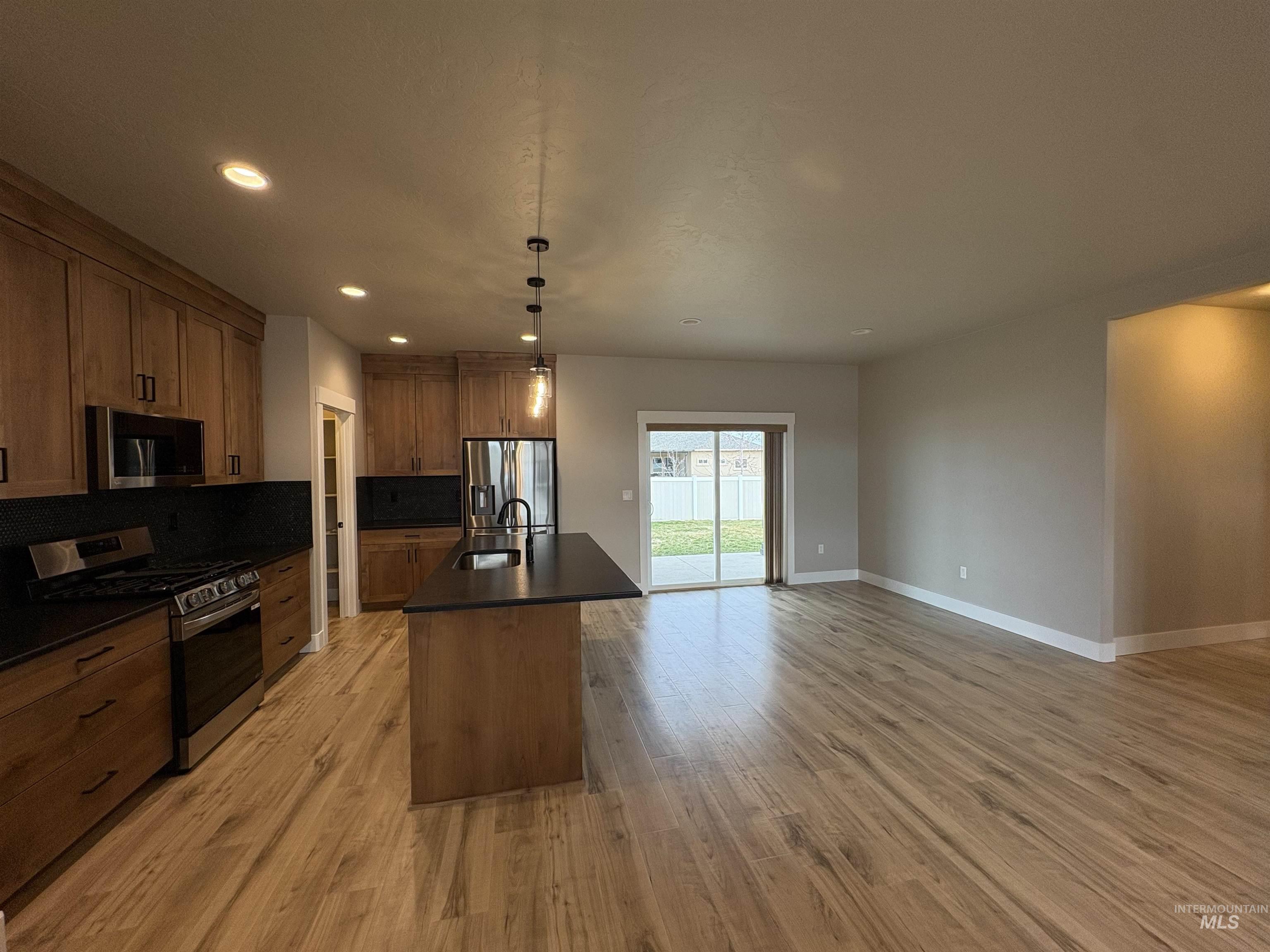 2184 Austin Way Fruitland, ID 83619 - Photo 11 of 34 Kitchen featuring stainless steel appliances, dark countertops, a kitchen island with sink, backsplash, and light wood-type flooring