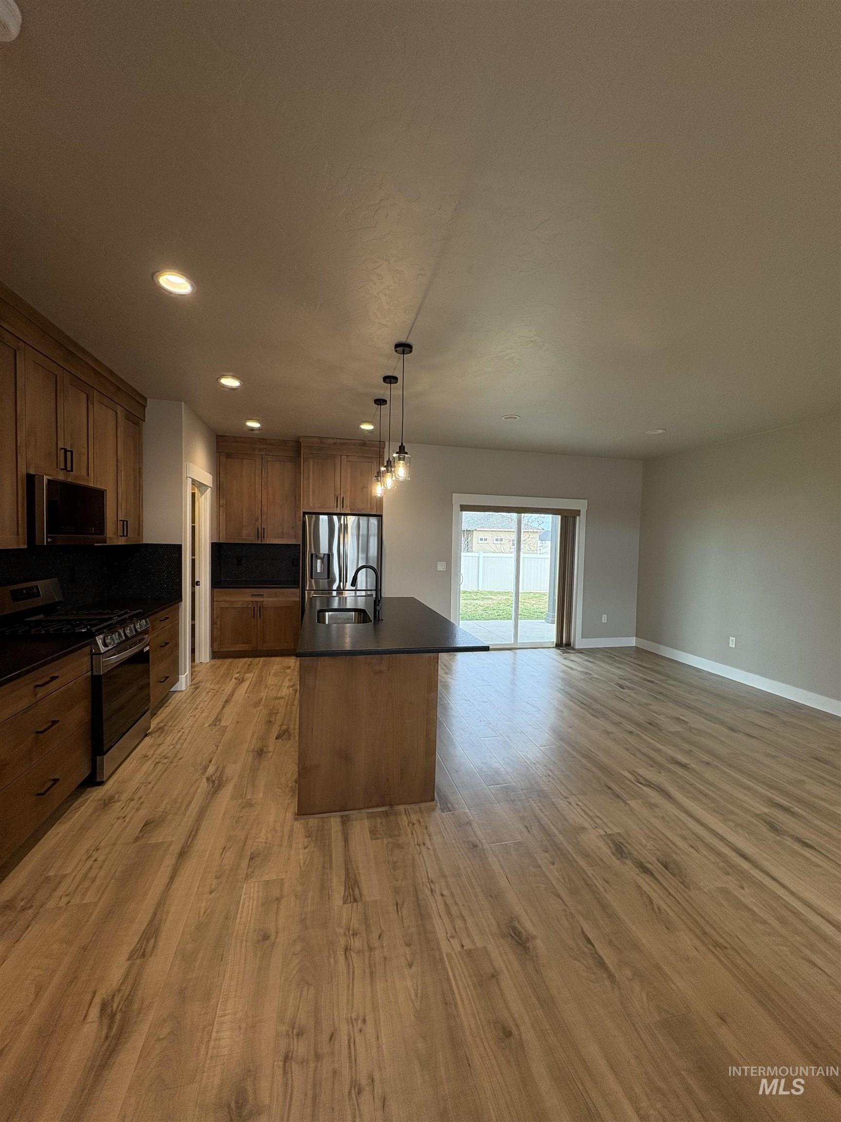 2184 Austin Way Fruitland, ID 83619 - Photo 12 of 34 Kitchen with stainless steel appliances, a center island with sink, wood finish cabinetry, decorative light fixtures, and light wood finished floors