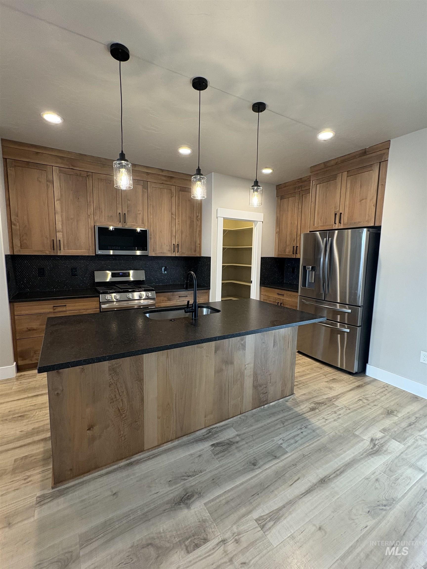 2184 Austin Way Fruitland, ID 83619 - Photo 13 of 34 Kitchen with wood finish cabinets, stainless steel appliances, an island with sink, pendant lighting, and tasteful backsplash