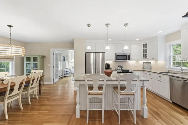 a kitchen with stainless steel appliances kitchen island granite countertop a dining table chairs and white cabinets