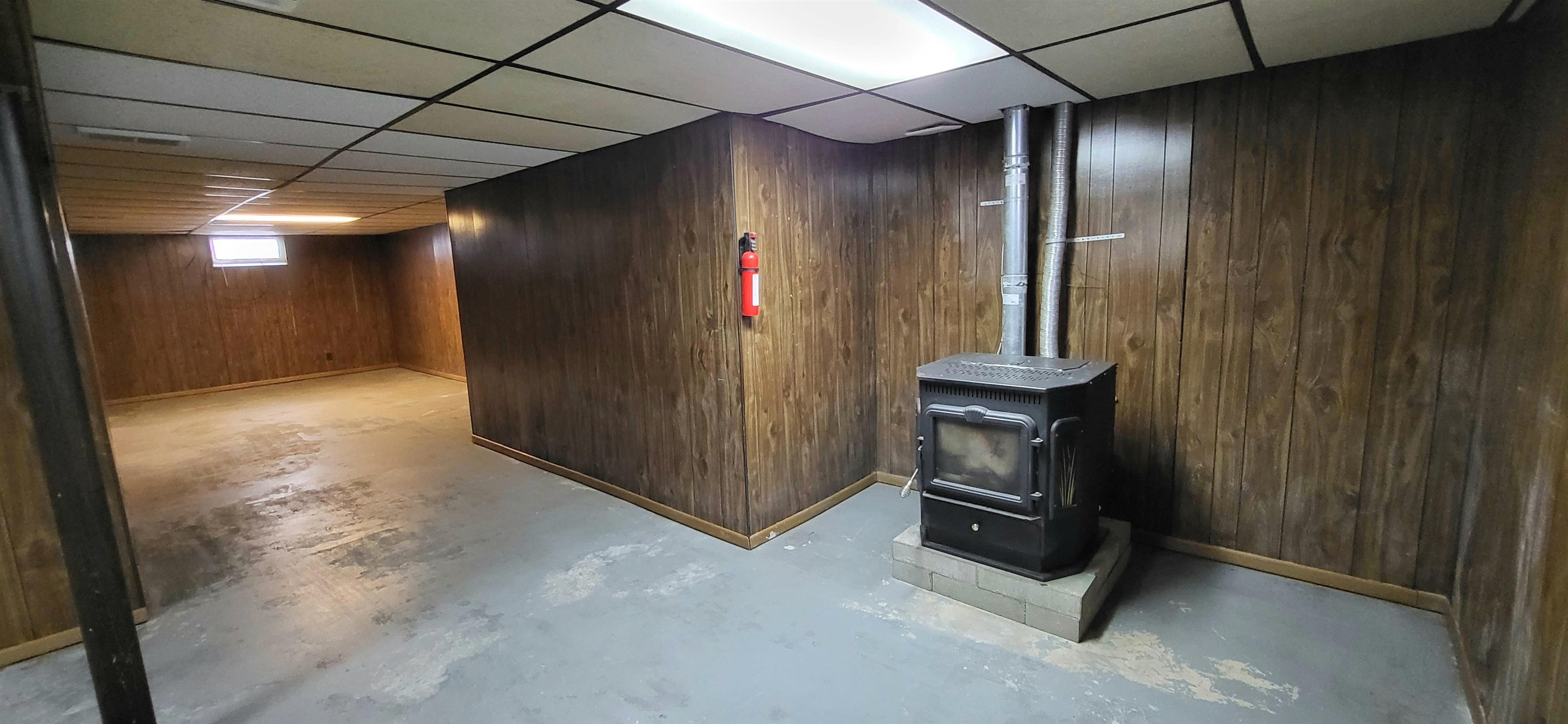 207 East 3rd Street Superior, WI 54880 - Photo 19 of 22 Below grade area featuring wood walls, a wood stove, and a paneled ceiling