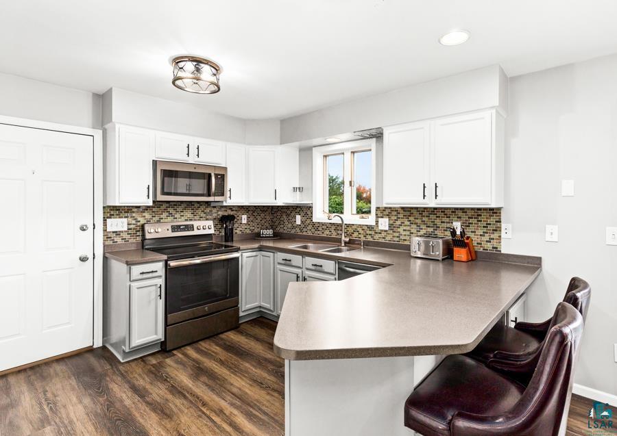 2020 East 11th Street Superior, WI 54880 - Photo 8 of 30 Kitchen with stainless steel appliances, dark wood finished floors, a peninsula, a breakfast bar, and white cabinets