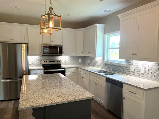 a kitchen with kitchen island granite countertop a sink appliances a counter space and cabinets